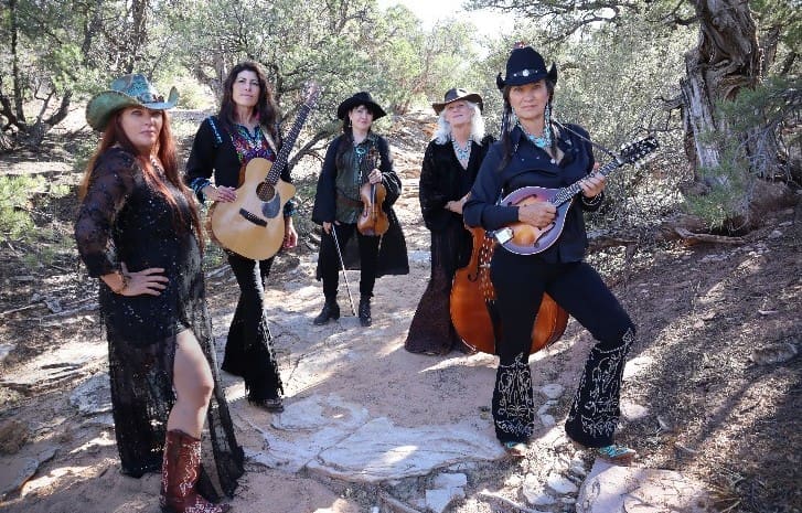 five women dressed in black with musical instruments in a natural dry stream bed