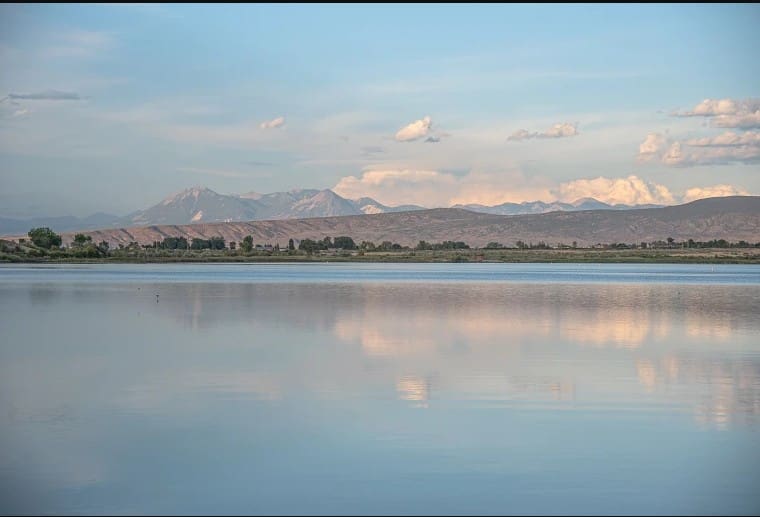 Panoramic view of Sweitzer Lake with distant mountains and white clouds reflecting on the calm blue water.
