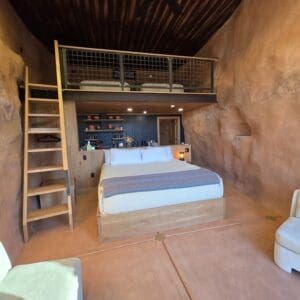 inside of a cave suite with red rock walls, a white bed and a loft with a ladder